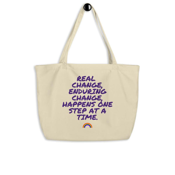 Cream organic tote bag with purple “Real Change, Enduring Change...” slogan and rainbow graphic