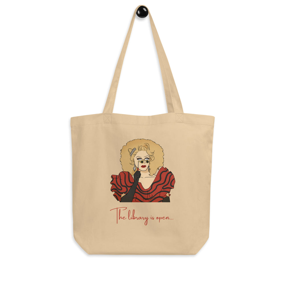 Front view of a beige tote bag with a drag performer illustration and “The library is open...” text