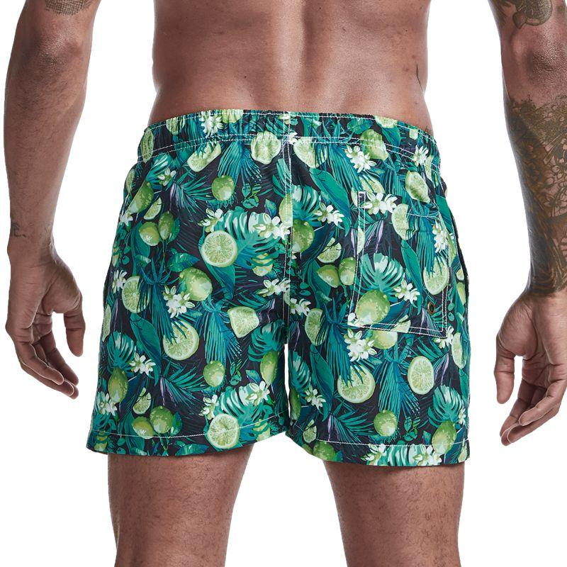 Rear view of green tropical-print board shorts with limes, leafy foliage, and a back pocket