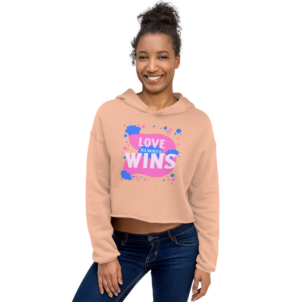 Smiling model wearing a peach cropped hoodie reading “LOVE ALWAYS WINS”