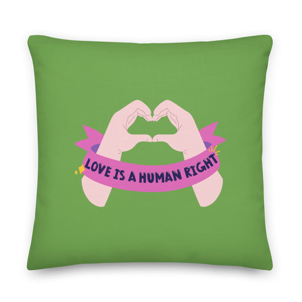 Green square pillow with illustrated hands forming a heart and a pink banner reading “LOVE IS A HUMAN RIGHT”