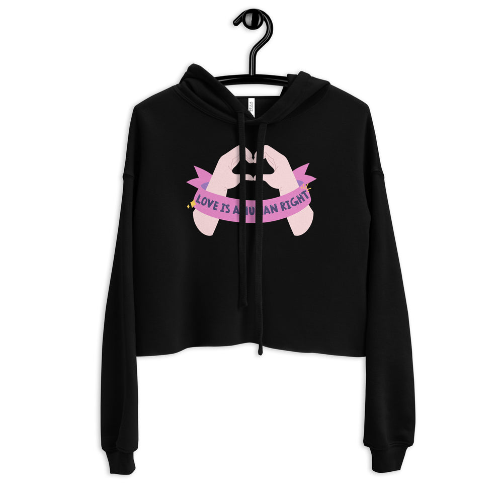 Front view of a black cropped hoodie on a hanger with a pink “LOVE IS A HUMAN RIGHT” graphic
