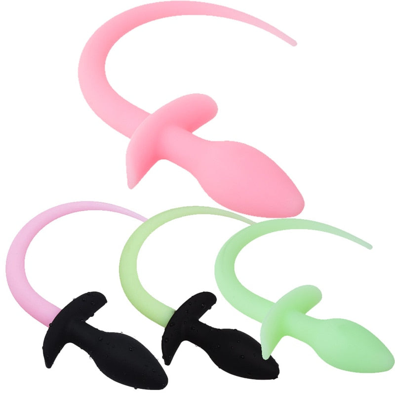 Three silicone dog-tail butt plugs in pink, black, and pale green, shown on white