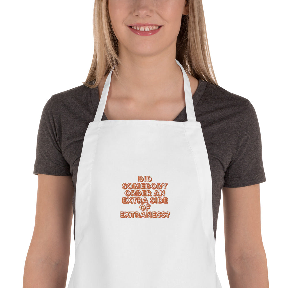 White embroidered apron reading “Did somebody order an extra side of extraness?” worn by a model