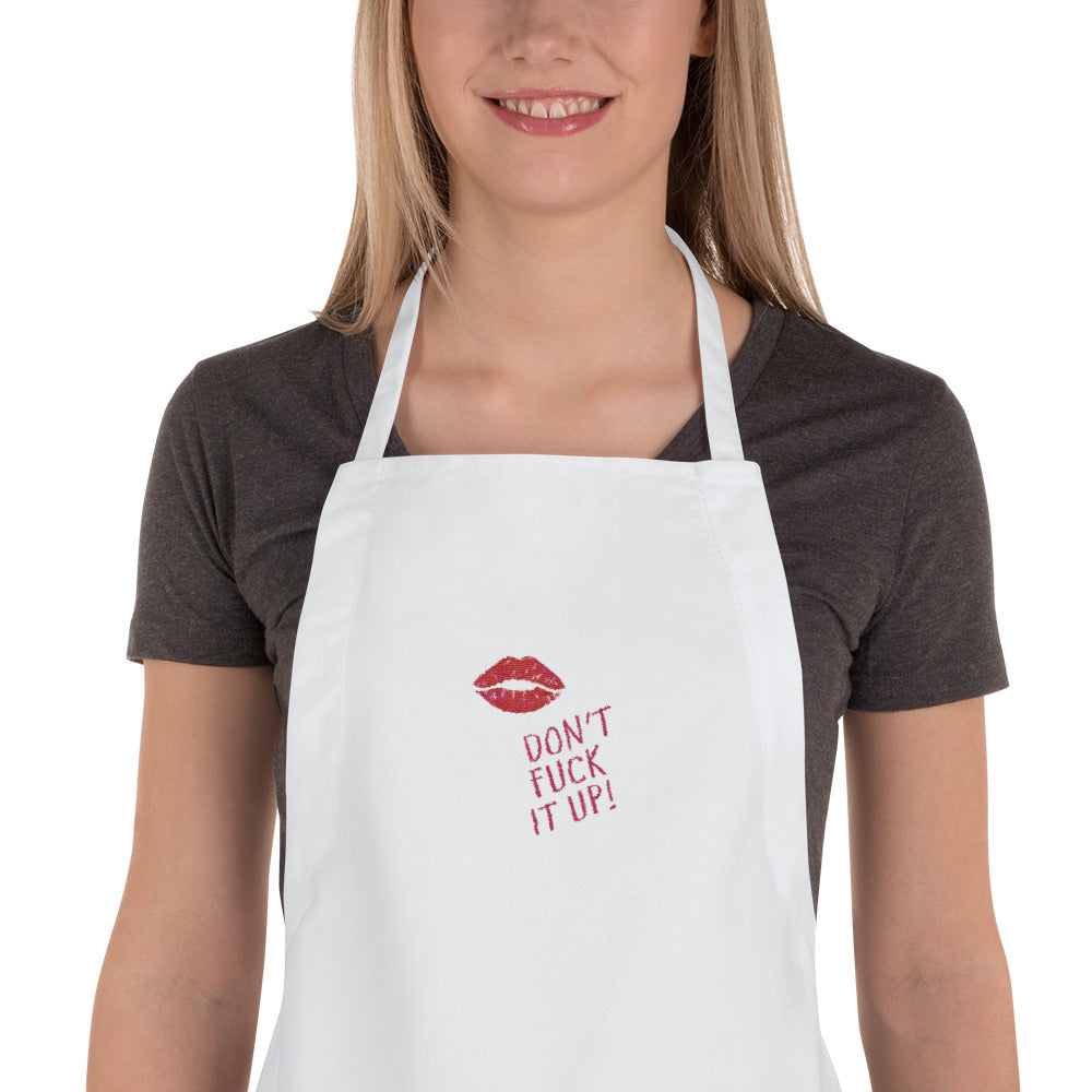 White embroidered apron with red lips and “DON’T FUCK IT UP!” slogan, worn by a model