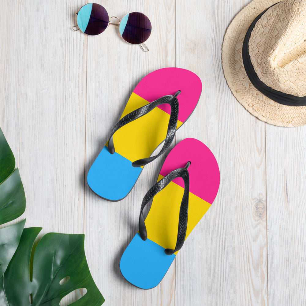 Pansexual Pride flip-flops with pink, yellow, and blue color-blocked soles on a wood surface