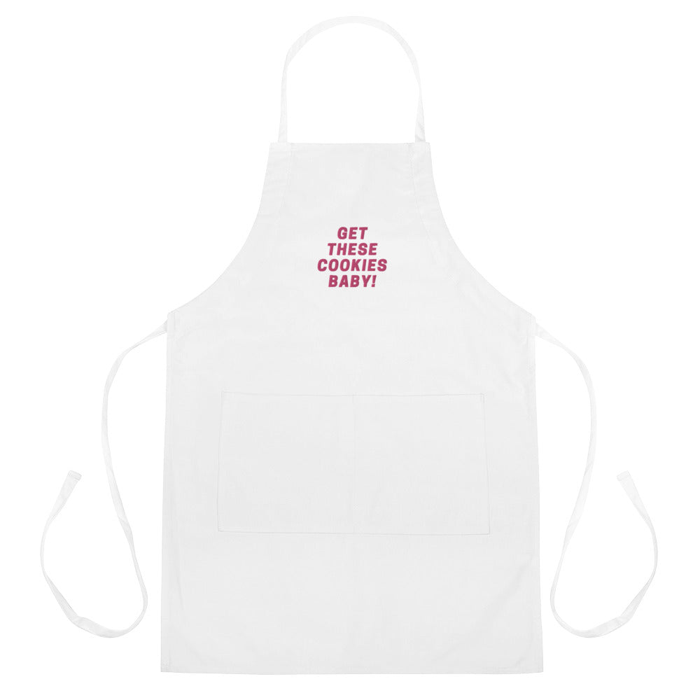 White apron with neck and waist ties, front pocket, and pink “GET THESE COOKIES BABY!” text