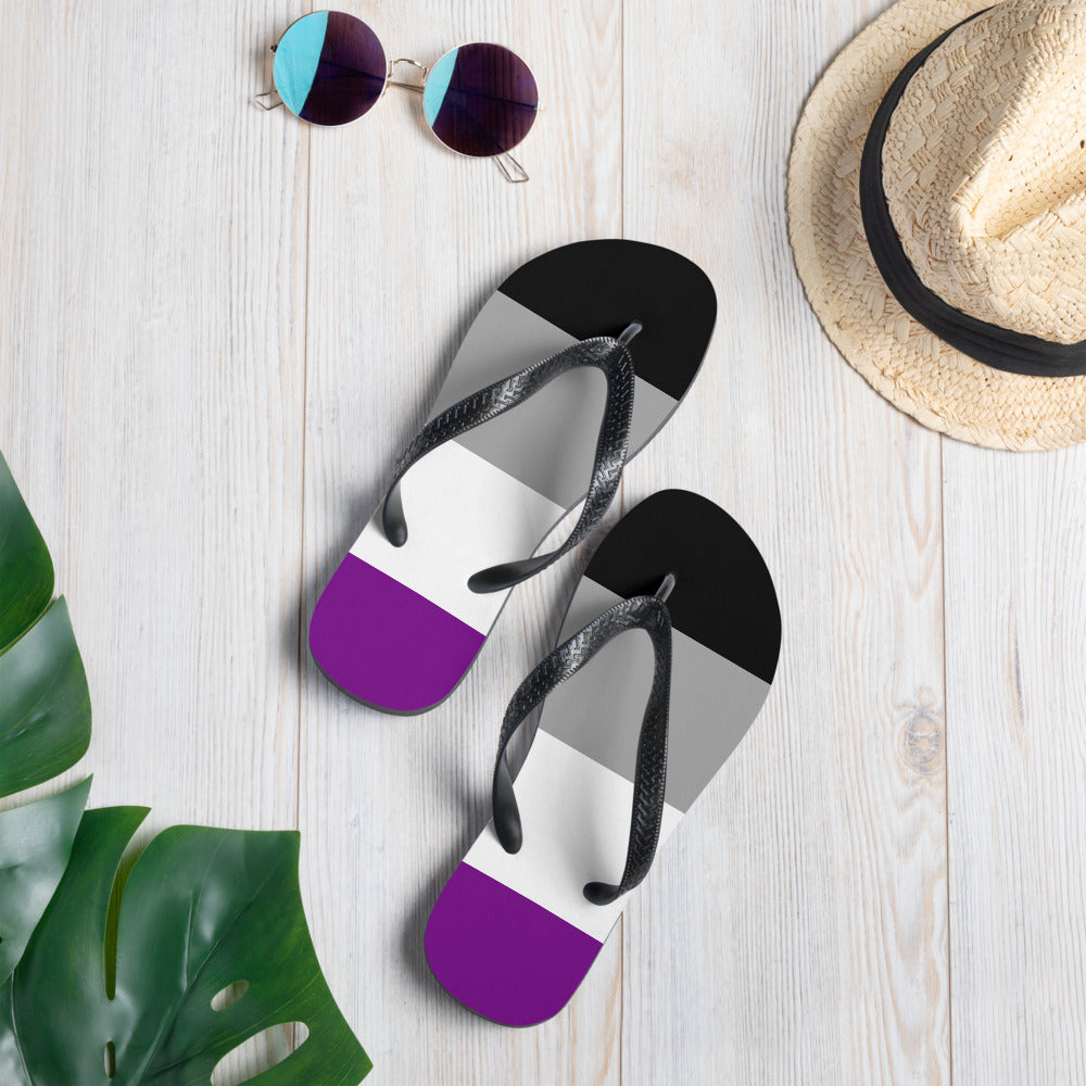 Asexual pride flip-flops with black, gray, white, and purple stripes on a wood surface