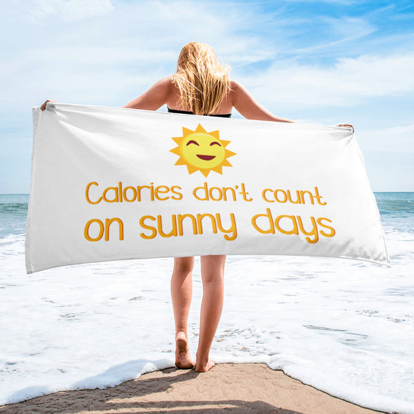 White beach towel reading “Calories don't count on sunny days,” held at the seashore