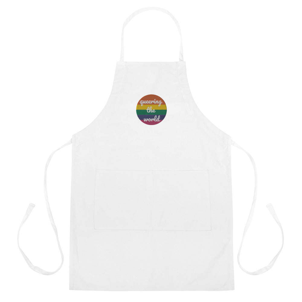 White embroidered apron with a rainbow badge reading “queering the world” and front pocket