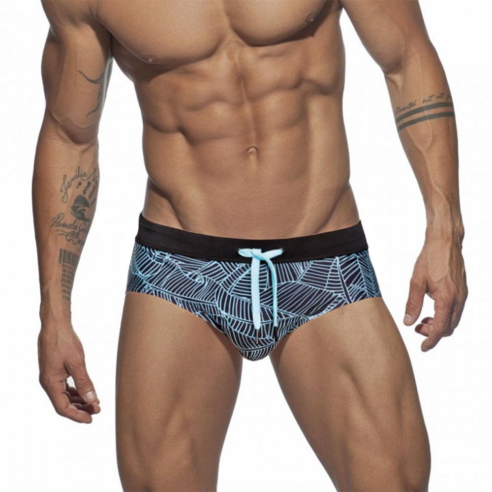 Close-up of a model wearing black swim briefs with a light blue geometric leaf print and drawstring