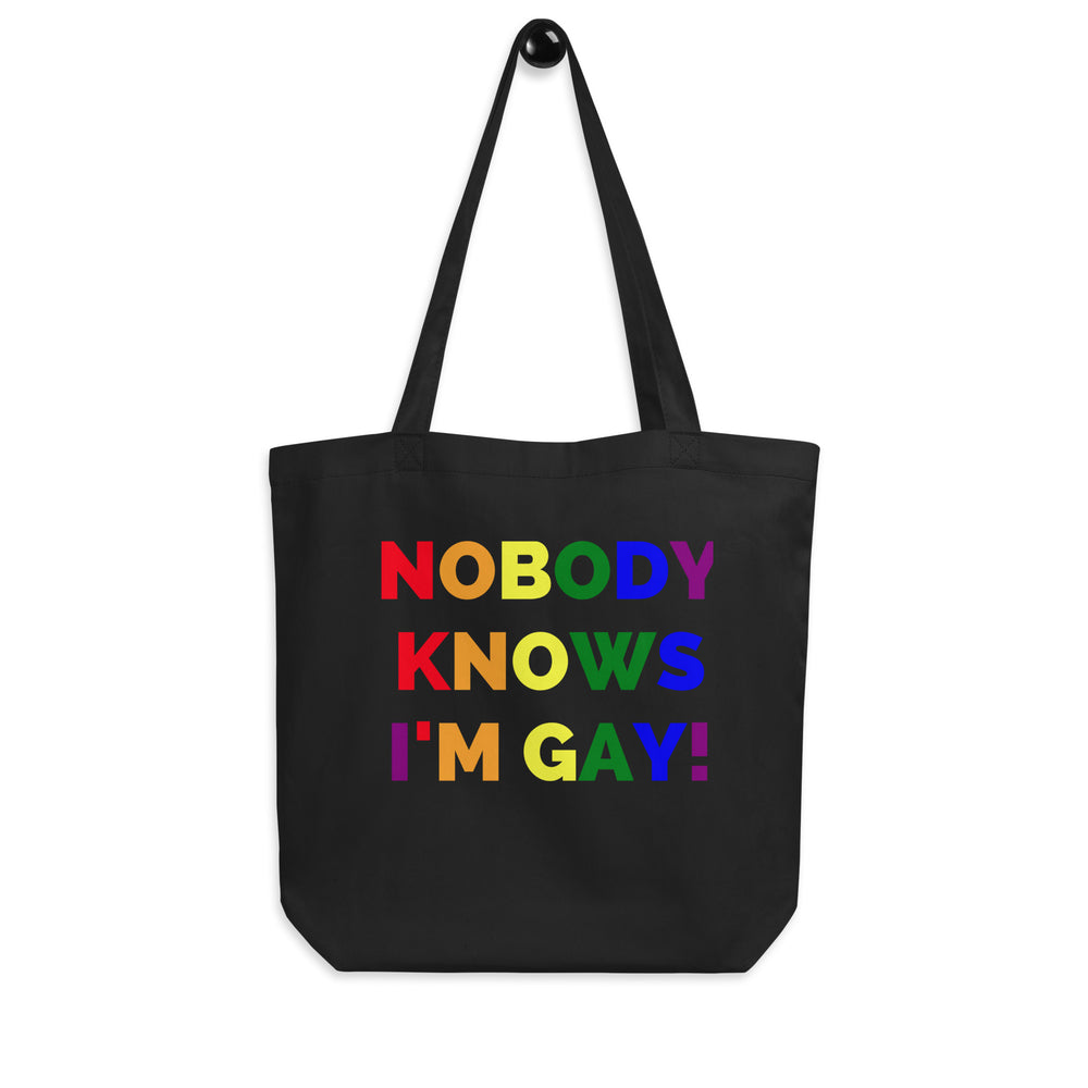 Front-facing black tote bag with rainbow lettering reading “NOBODY KNOWS I'M GAY!”