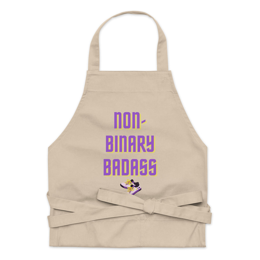Front-facing beige apron reading “NON-BINARY BADASS,” with purple and yellow lettering and sneaker graphic