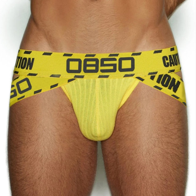 Model wearing a yellow ÖBSO caution jockstrap with black warning-strip lettering