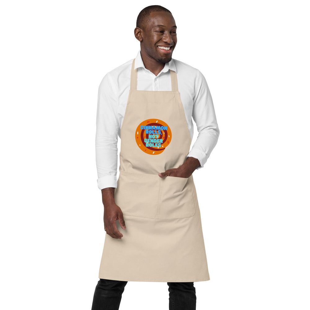 Model wearing a beige apron with a cinnamon-roll graphic and “CINNAMON ROLLS, NOT GENDER ROLES” text
