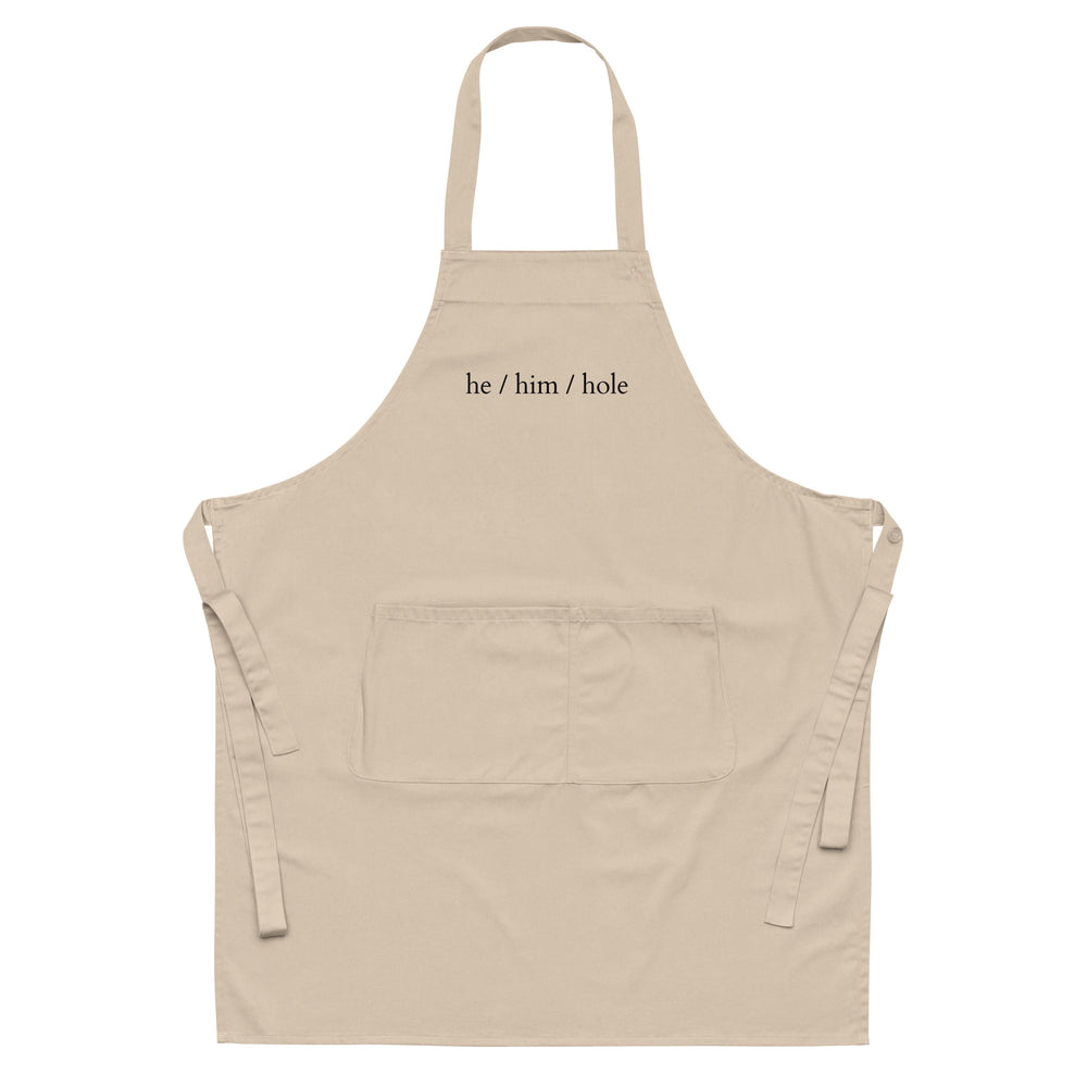 Front view of a beige apron with a divided pocket and “he / him / hole” text