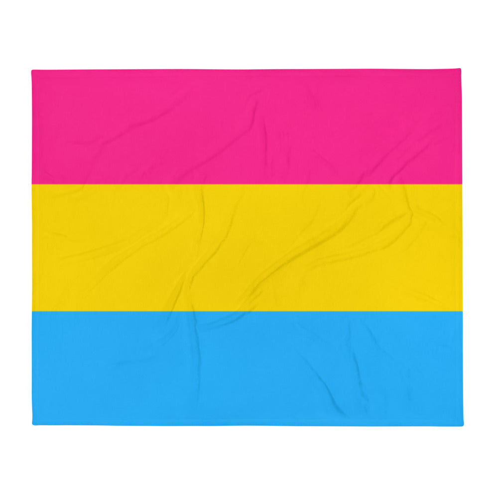 Pansexual Flag throw blanket with bold blue, yellow, and pink stripes wraps a smiling woman relaxing on a bed; soft room lighting.