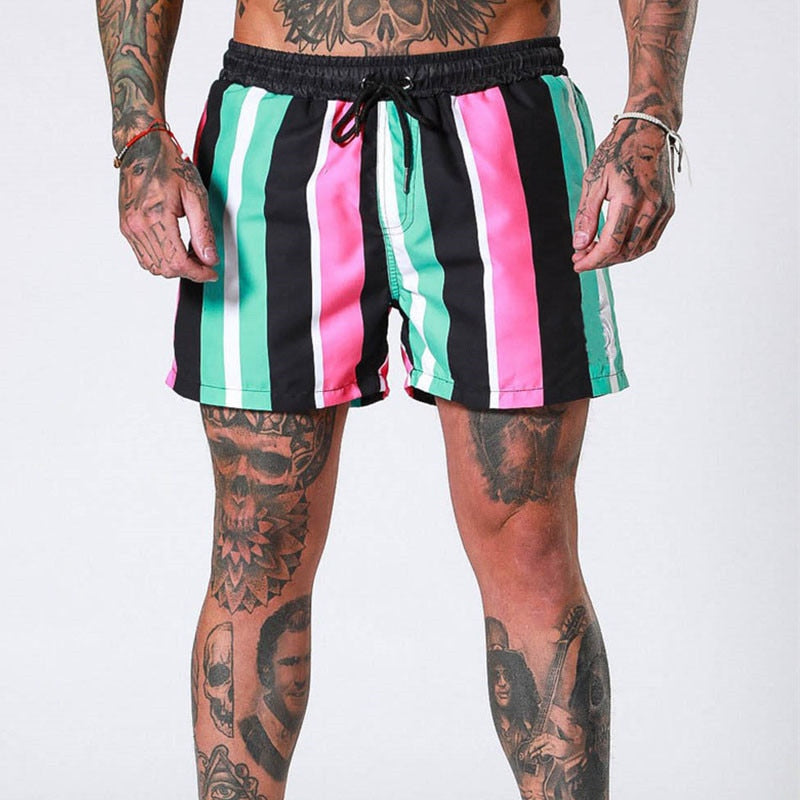 Front view of black shorts with vertical pink, mint, and white stripes on a tattooed model