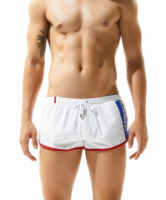 Front-view model wearing white gym shorts with red trim and blue side lettering