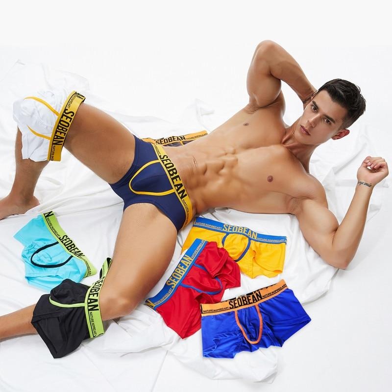 Navy boxer briefs with yellow trim and SEOBEAN waistband, modeled with colorful boxer briefs on a bed