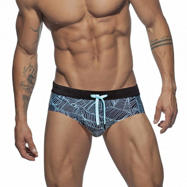 Close-up of a model wearing black swim briefs with a light blue geometric leaf print and drawstring