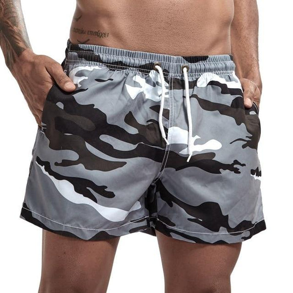 Model wearing gray, black, and white camouflage swim shorts with drawstring waist and side pockets