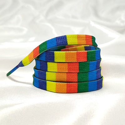 Coiled rainbow-striped shoelaces with blue-tipped ends on white fabric