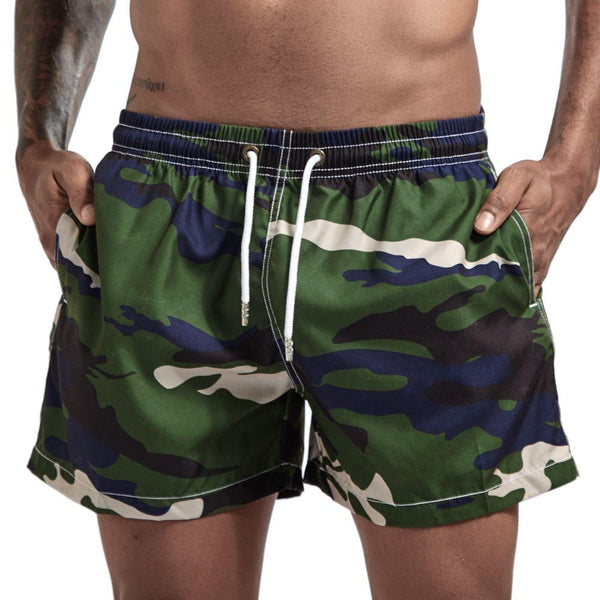 Green camouflage board shorts with white drawstring and side pockets, worn by a model