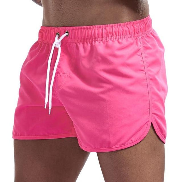 Bright pink swim shorts with white drawstring and curved split hems