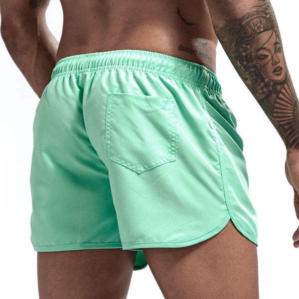 Mint green swim shorts shown from the rear with an elastic waistband, back pocket, and side slits