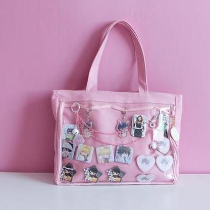 Pink transparent canvas tote displaying enamel pins and dangling charms against a pink backdrop