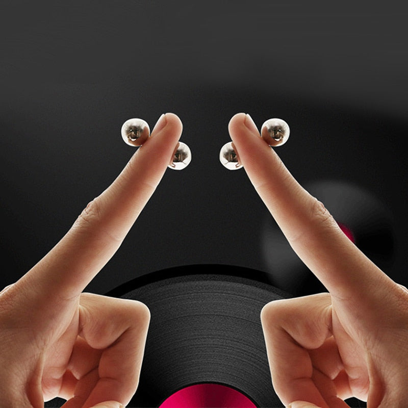 Two hands hold matching silver magnetic nipple balls against a black background