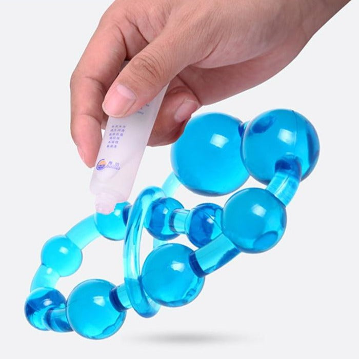Hand holding a tube of lubricant over bright blue silicone anal beads