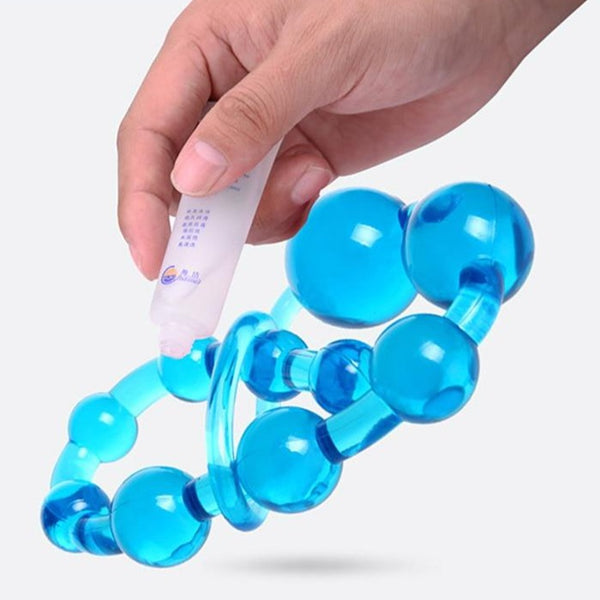 Hand holding a tube of lubricant over bright blue silicone anal beads