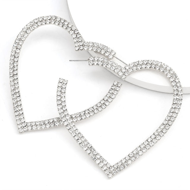 Heart-shaped hoop earrings covered in clear rhinestones, shown crossed on a white background