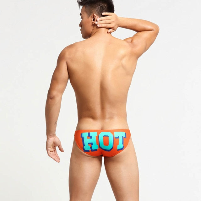 Rear-view model wearing orange briefs with large blue-and-red “HOT” lettering