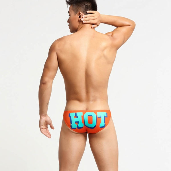 Rear-view model wearing orange briefs with large blue-and-red “HOT” lettering