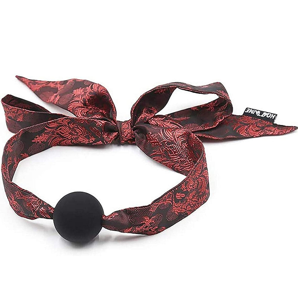 Black ball gag with red patterned satin straps arranged on a white background