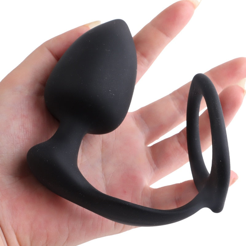 Black silicone cock ring with attached butt plug held across an open hand
