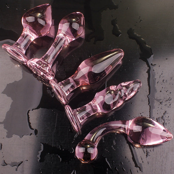 Five translucent pink glass butt plugs arranged on a wet dark surface