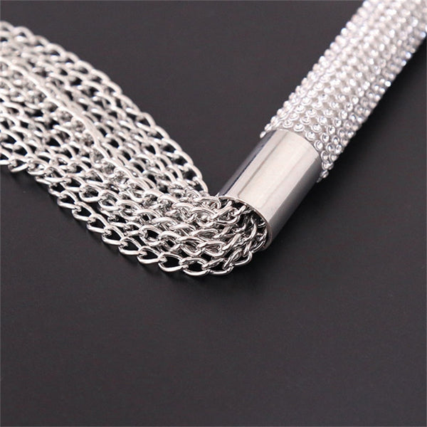 Close-up of a silver chain whip with a textured handle on a dark surface