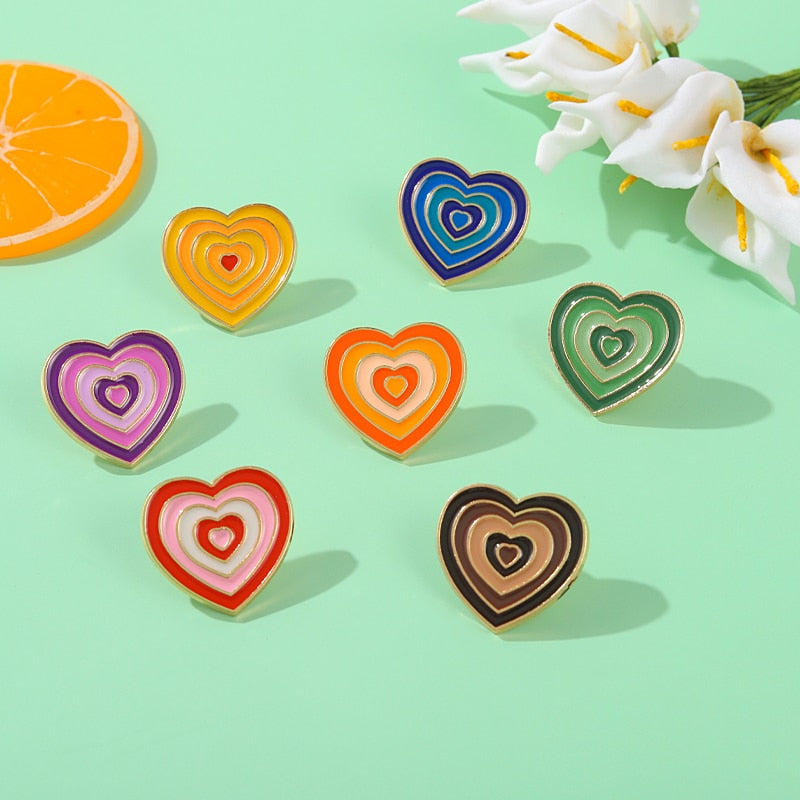 Flat lay of seven colorful heart-shaped enamel pins on a mint-green surface
