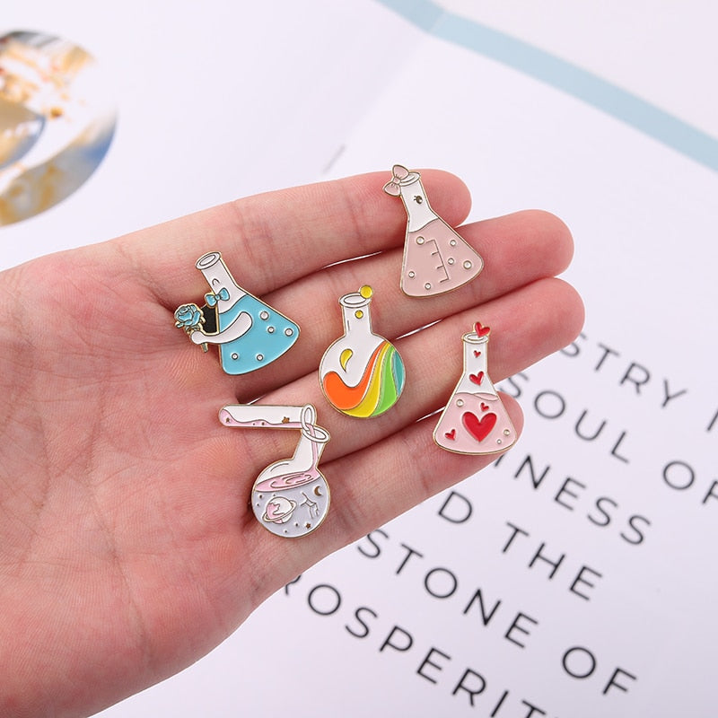 Hand displaying five colorful enamel pins shaped like potion flasks
