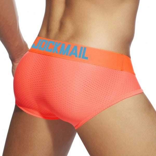 Close-up rear view of a model wearing neon coral mesh briefs with a blue JOCKMAIL waistband