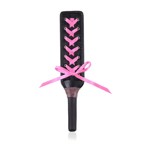 Black lace-up BDSM paddle with pink ribbon bow on a white background