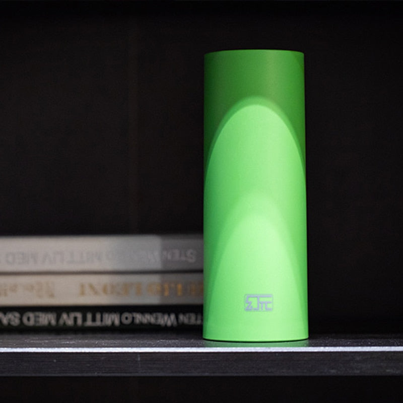 Bright green cylindrical penis sleeve standing on a shelf beside stacked books