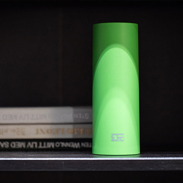 Bright green cylindrical penis sleeve standing on a shelf beside stacked books