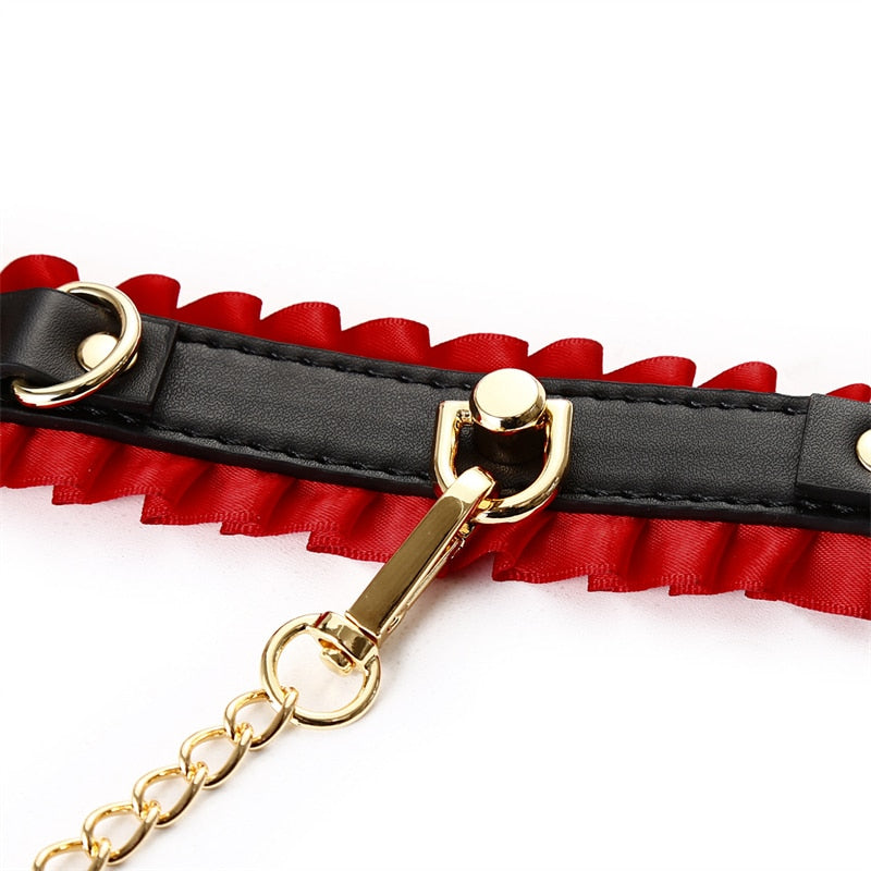 Close-up of a black leather collar with red ruffles, gold hardware, and attached chain