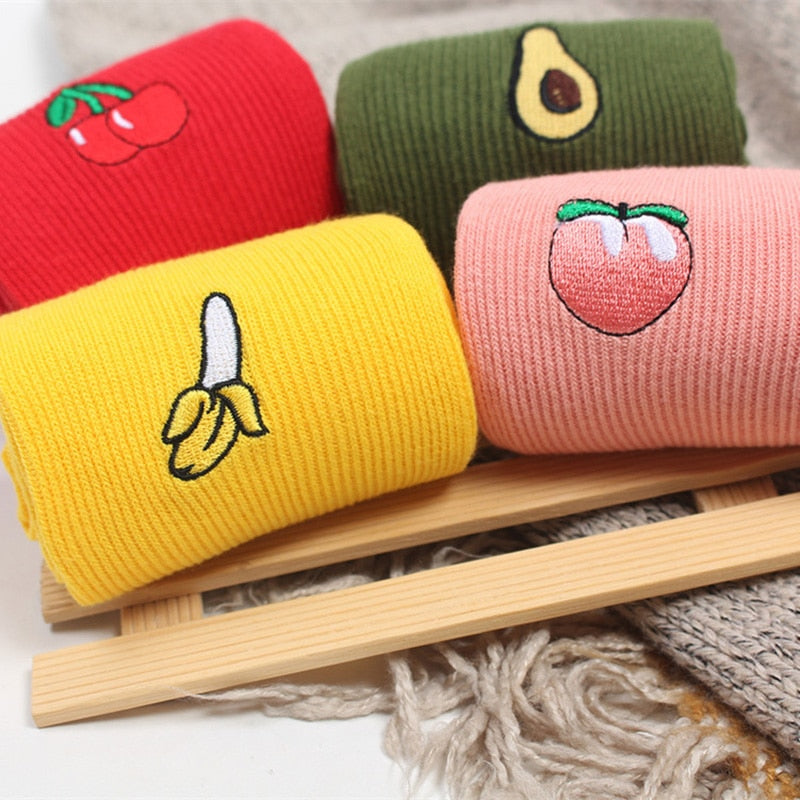 Four rolled socks with cherry, avocado, tomato, and banana motifs on a wooden rack