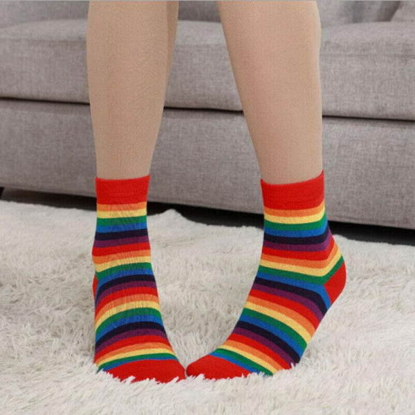 Person wearing rainbow-striped crew socks while standing on a white rug